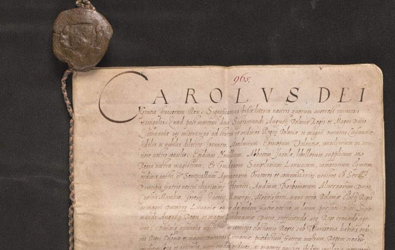 Starożytny pergamin z ręcznym, łacińskim tekstem i dużym nagłówkiem "CAROLVS DEI", z widocznym pionowym zagięciem i śladami zabrudzeń, przywiązany po lewej stronie splecionym sznurkiem do dwóch dużych okrągłych ciemnobrązowych pieczęci, leżący na czarnym tle; widoczne także czerwony numer "965" u góry i ołówkowy zapis "575" u dołu.